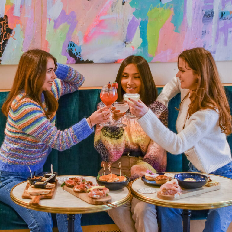 3 jeunes femmes trinquant en souriant prête à passer une soirée mémorable. Cocktails, tapas, à déguster sans modération.