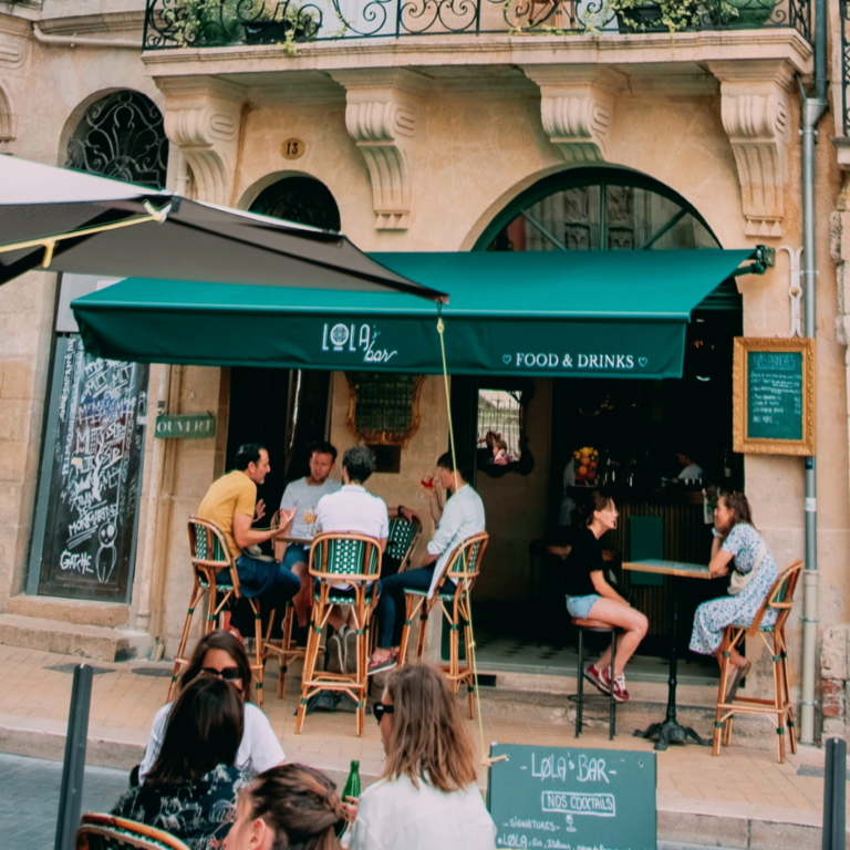 Vue extérieure du LOLA’s Bar avec sa terrasse remplie de clients, mettant en avant son ambiance chaleureuse et animée.