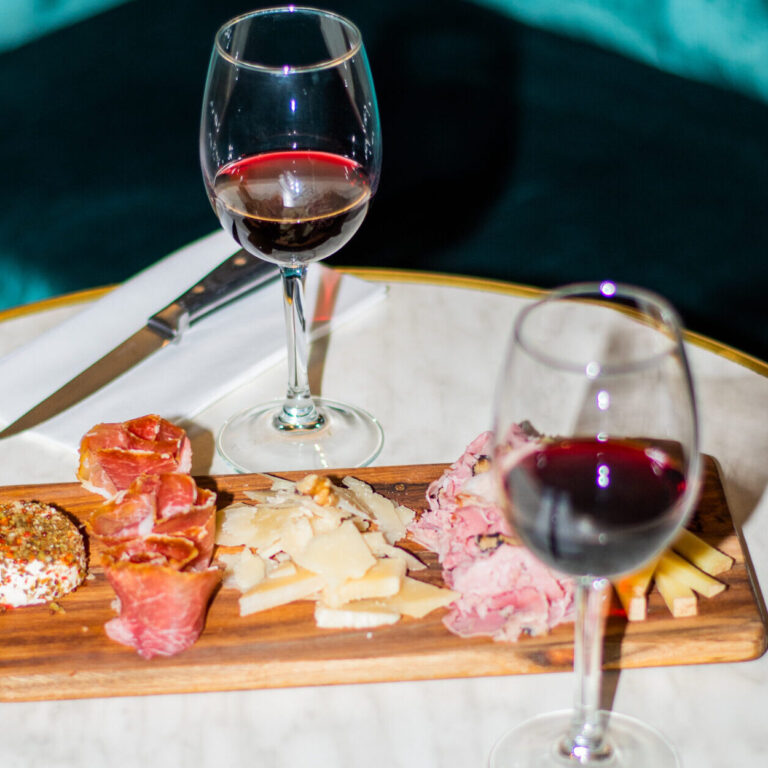 Table élégamment dressée avec deux verres de vin rouge et une planche de tapas, illustrant l’expérience culinaire du LOLA’s Bar.