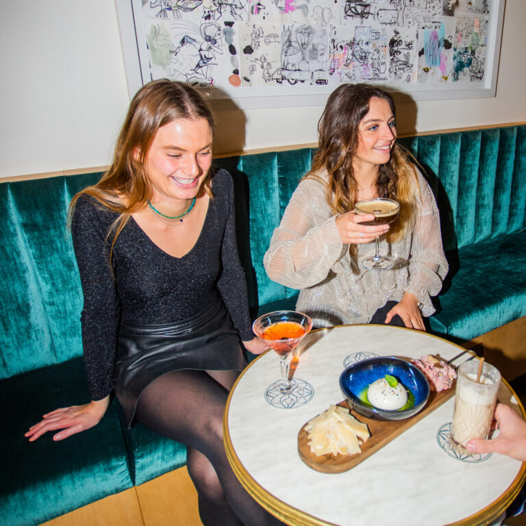 Deux femmes partageant un verre et une planche de tapas dans l’ambiance cosy du LOLA’s Bar à Bordeaux.