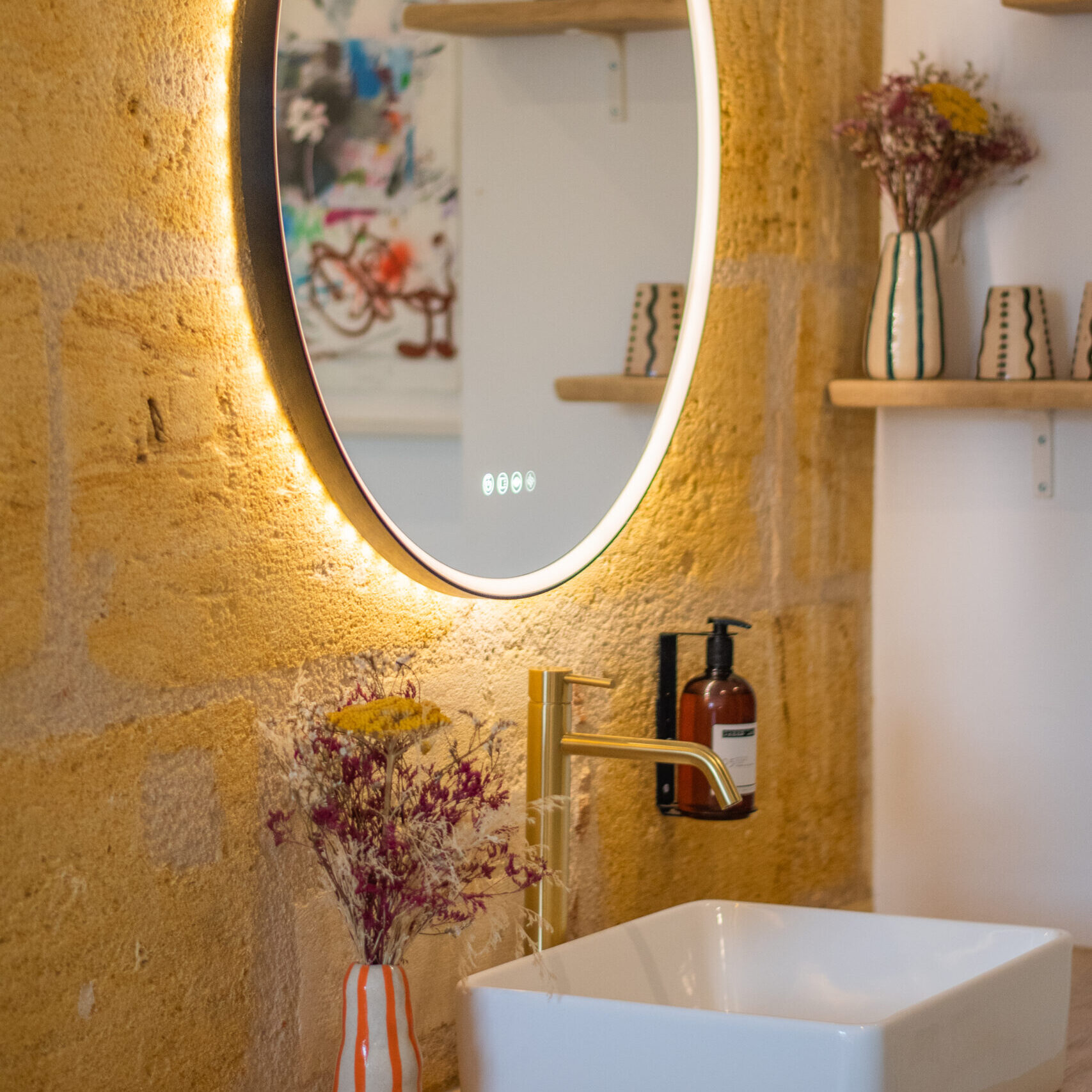 Miroir rond avec cadre doré sur un mur en pierre, accompagné d’une décoration chaleureuse dans une chambre de l’hôtel LOLA O-Collection.