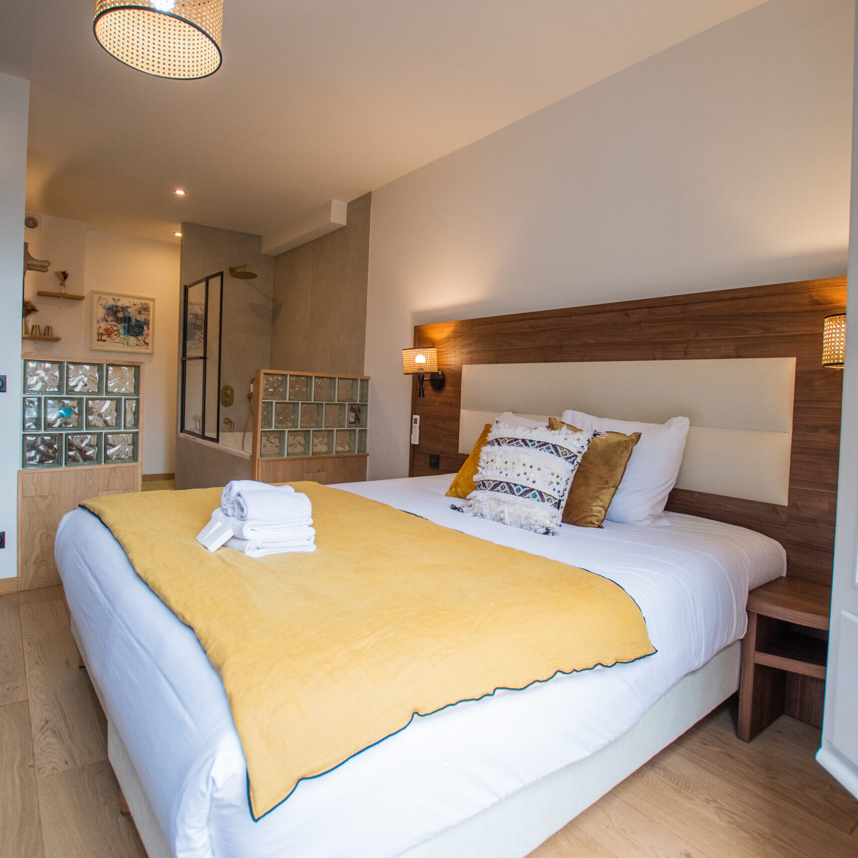 Chambre spacieuse et lumineuse avec lit confortable et coussins jaunes, offrant une atmosphère chaleureuse au boutique hôtel LOLA - O-Collection Bordeaux.